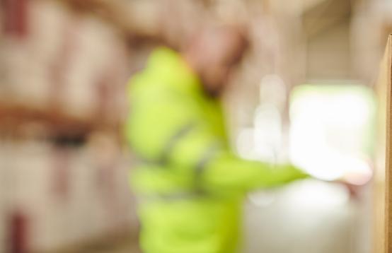 Photo of man in a warehouse wearing a Fluro jacket with a brown box with a recycling image 