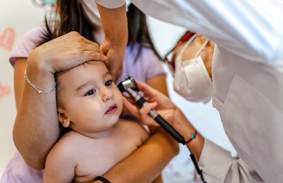 Nurse holding a baby checking the inside the baby's ear.