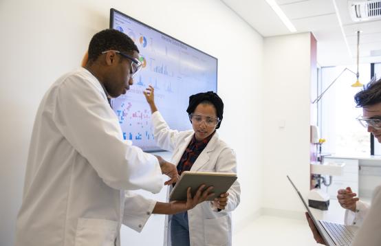 Three people in white lab coats in discussion in a laboratory. 