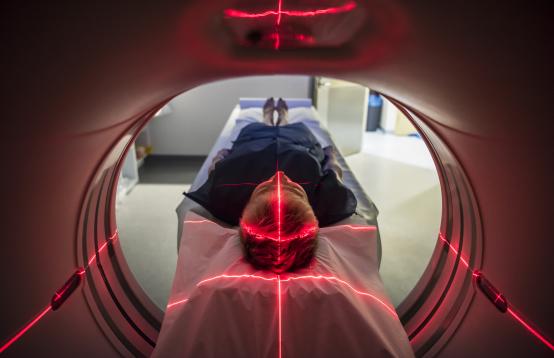 Image of a person being slid into a CT scan with red lights across the body.