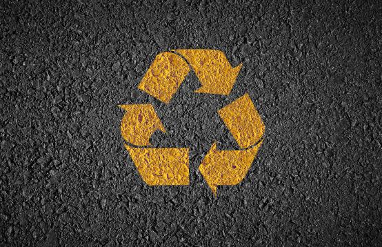 Image of a recycled road with a yellow recycling icon painted on in yellow.