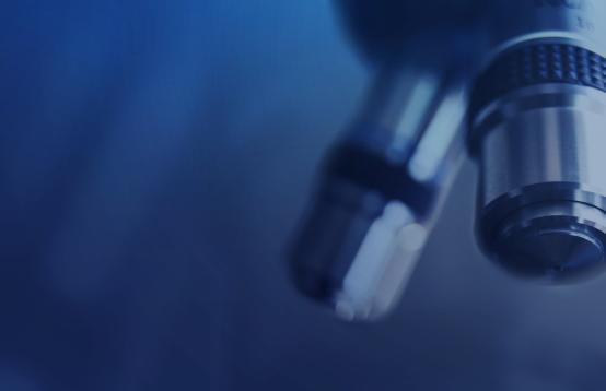 Close up photo of lenses on a microscope in a darkened blue room.