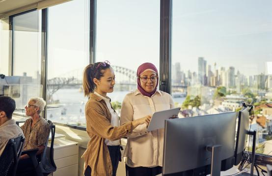 Two women having a discussion while looking at an ipad.