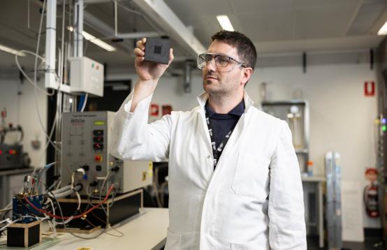 Dr Quentin Meyer holding fuel cell wearing a white coat and safty glasses.