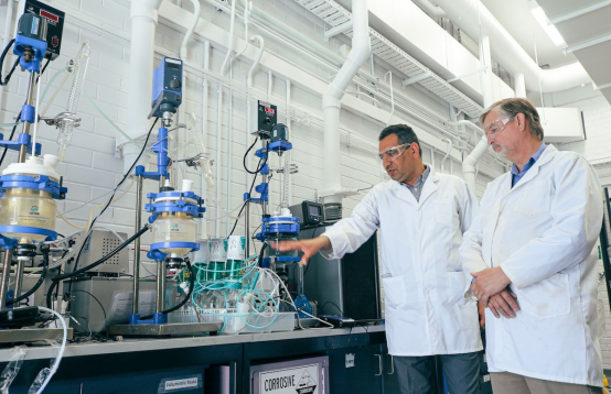 Image of two people wearing white coats and safety glasses in a laboratory.