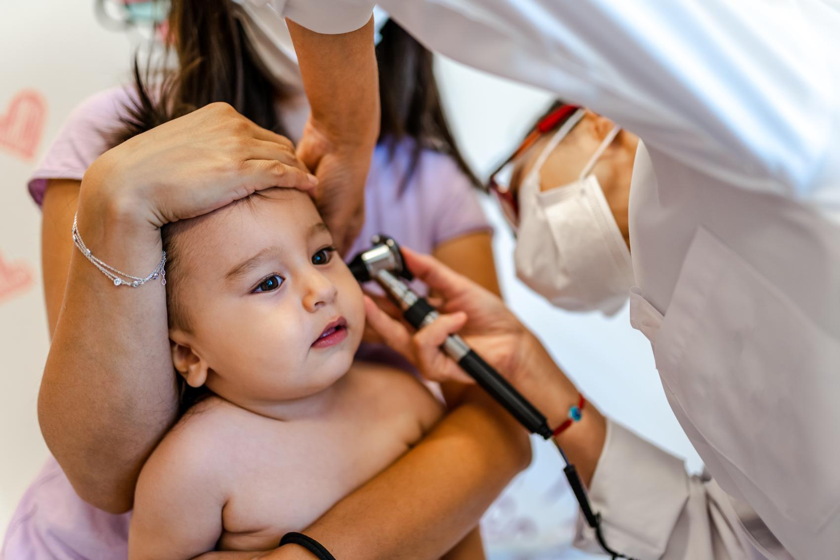 Nurse holding a baby checking the inside the baby's ear.