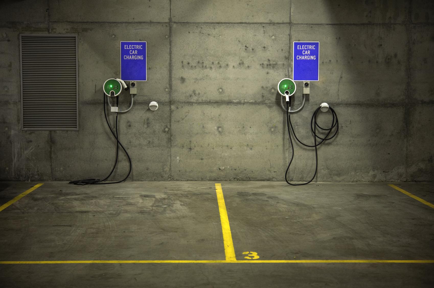 Two electric car charging stations in an underground parking station with blue signs and yellow lines on the ground marking car spaces.