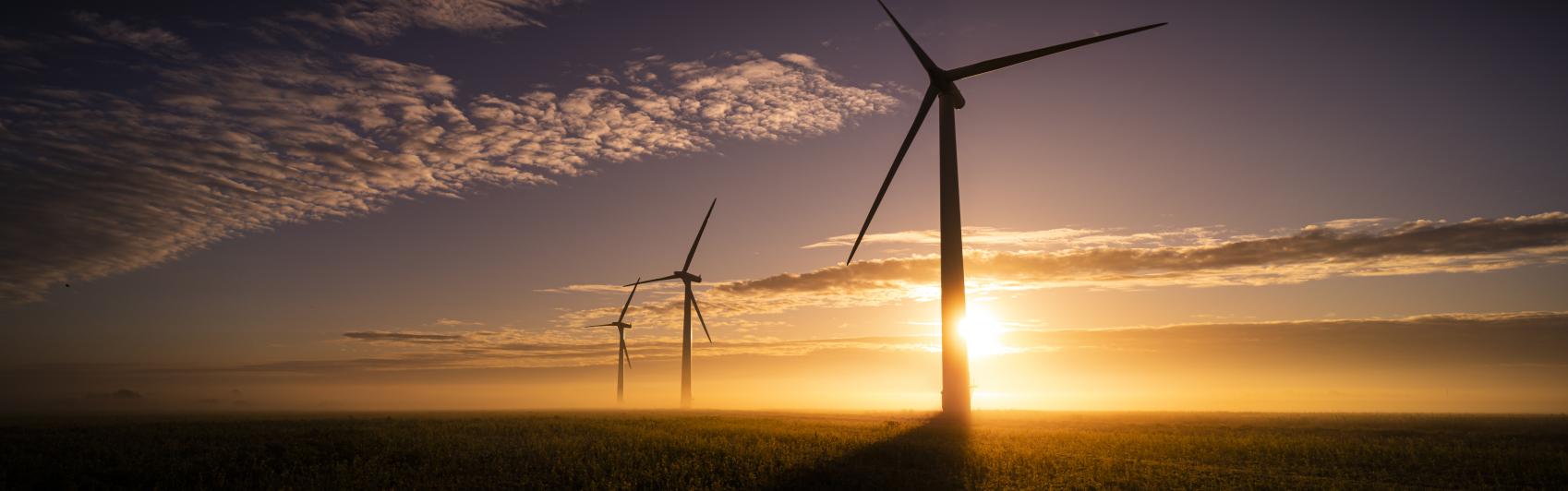 Image of a sunset with scattered clouds and windmills in the foreground.