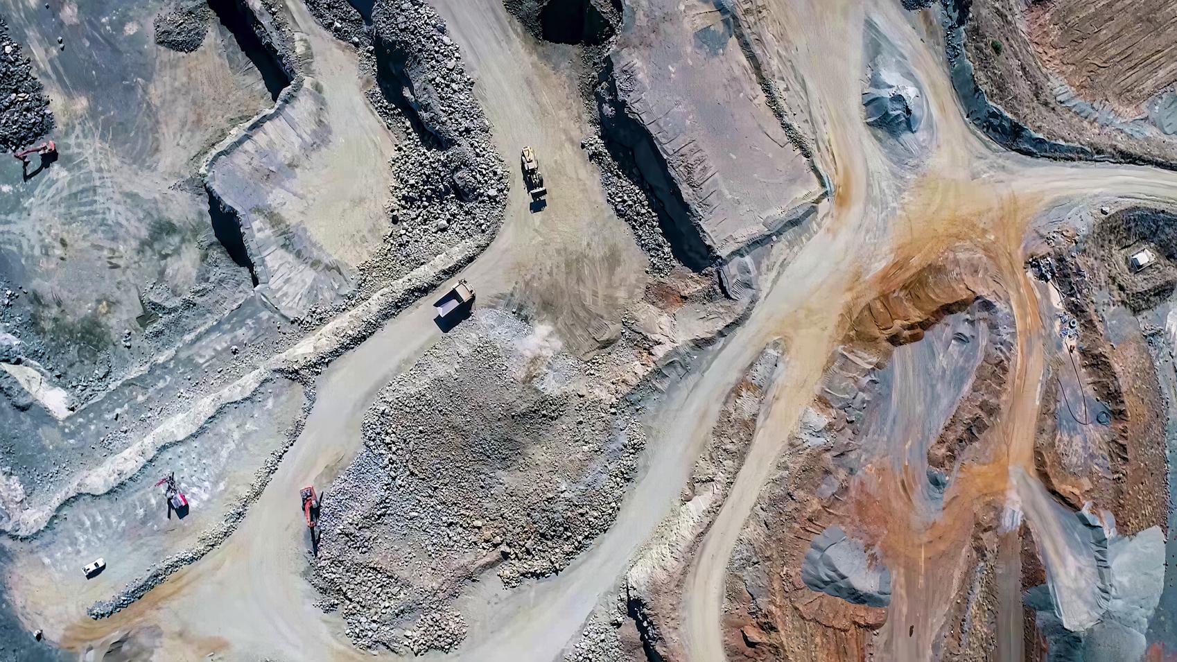 Areial view of a mining site with trucks and cars driving on the dirt roads.