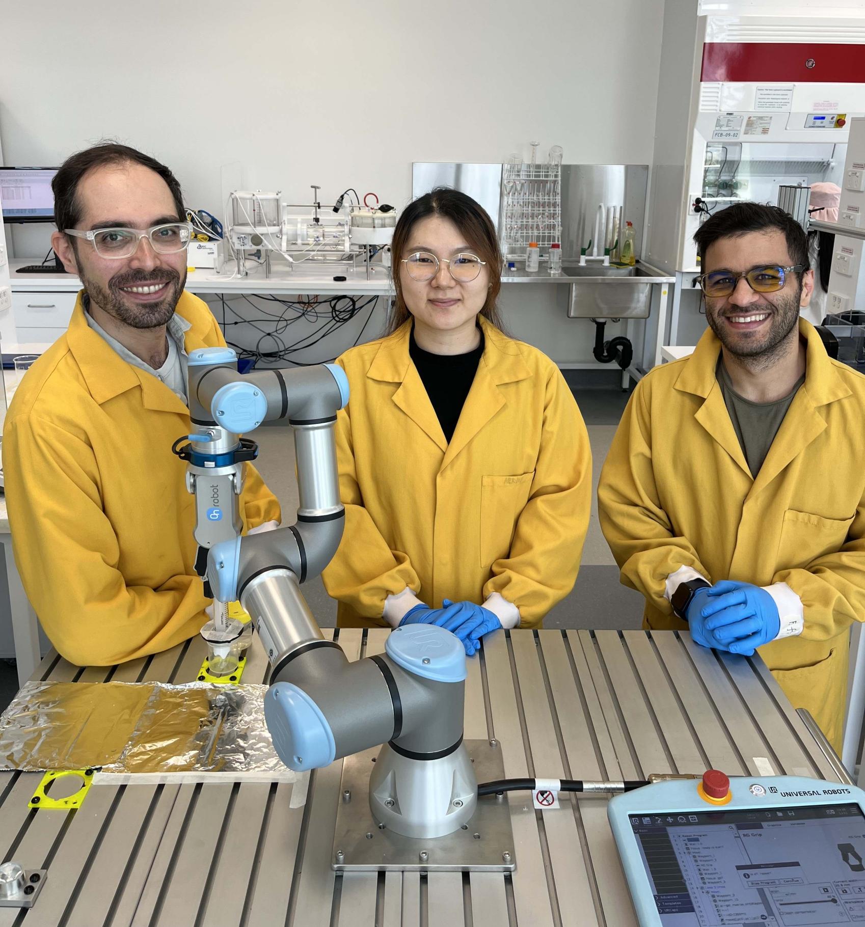 Three people standing in front of science equipment smiling