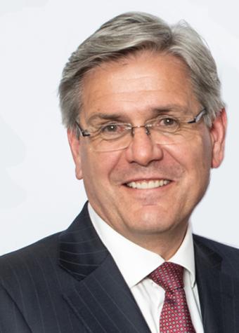 Photo of Jeff Connolly. A man wearing a dark suit, a white shirt and dark red tie and spectacles, with short grey hair smiling.