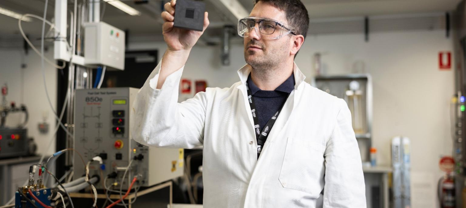 Dr Quentin Meyer holding fuel cell wearing a white coat and safty glasses.